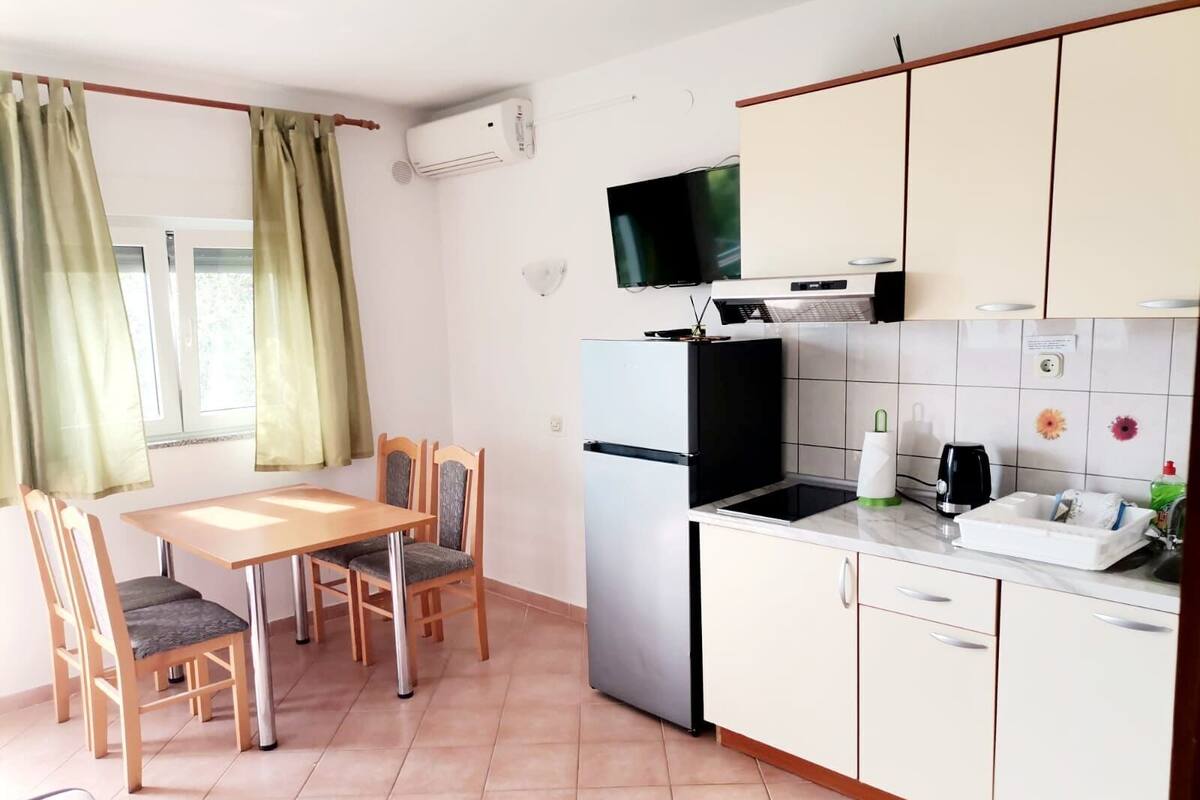 Eine kleine Küche mit Essbereich, einem Fernseher über dem Herd und einem Fenster mit Vorhängen.