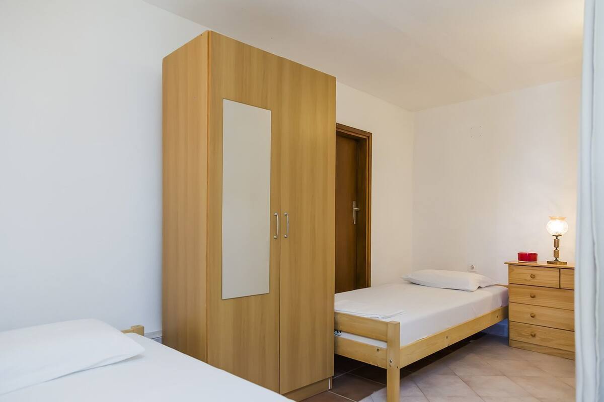 Ein Schlafzimmer mit einem Holzschrank, einem Einzelbett, einem Nachttisch mit Lampe und einer kleinen Kommode.