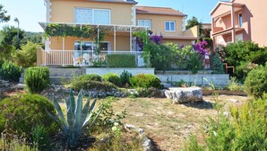 Une maison à deux étages dotée d’un balcon, entourée de différentes plantes et d’un jardin.