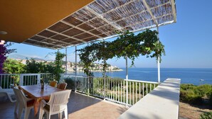 Une terrasse avec une table et des chaises, une pergola et une vue sur la mer et les bâtiments situés au loin.