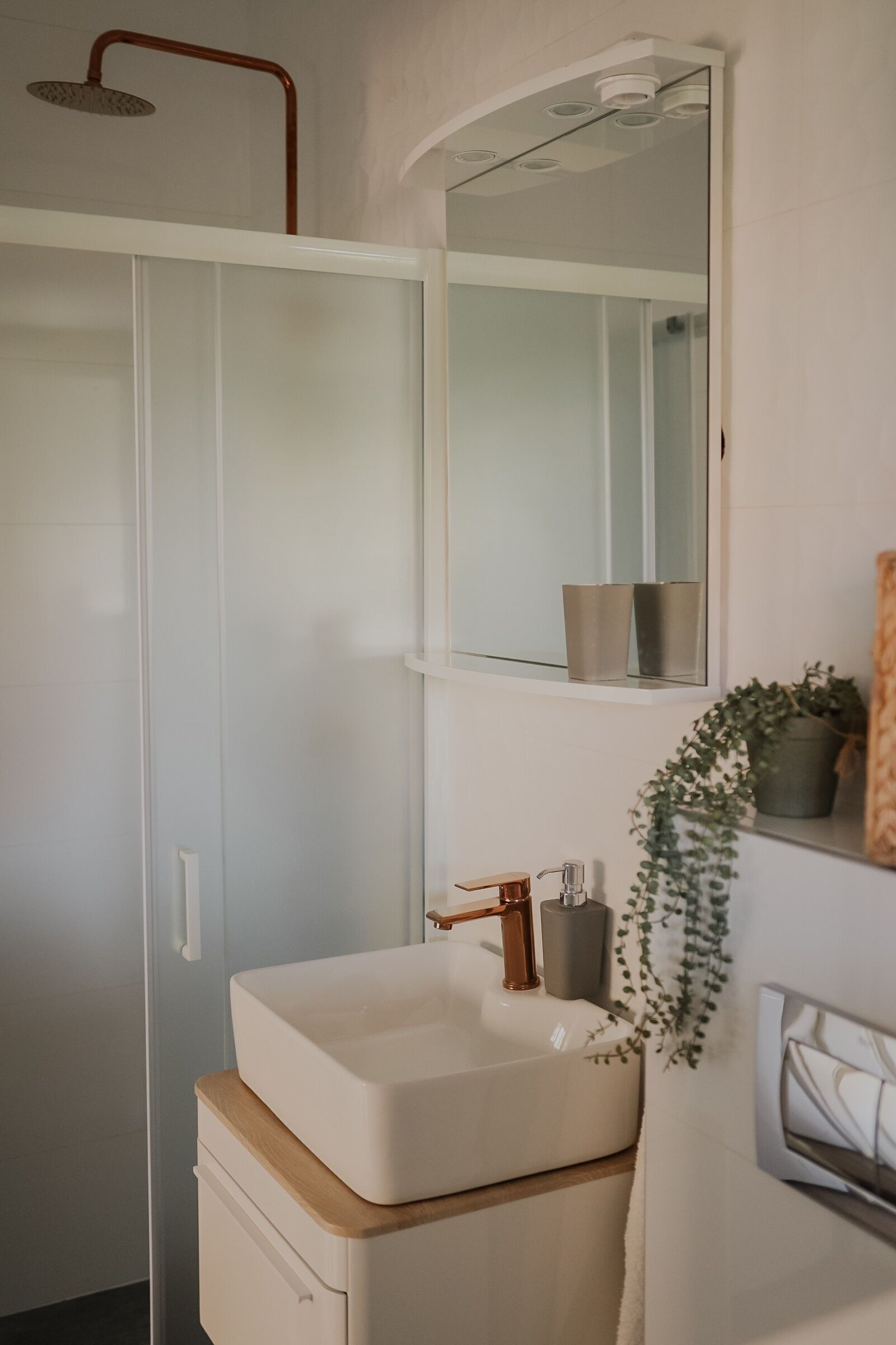Un baño moderno con un lavamanos blanco, un espejo y una ducha.
