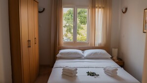 A bedroom with a bed, a wardrobe, a window with curtains, and a bedside lamp. - Apartments Prce (Orebic)