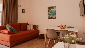 A living room with a red sofa, a dining table with chairs, a painting on the wall, and an air conditioning unit. - Apartments Prce (Orebic)