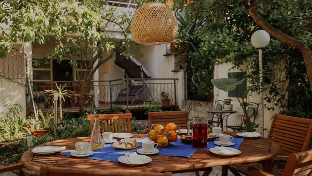 A round wooden table set for breakfast with plates, cups, and a fruit basket. - Apartments Prce (Orebic)