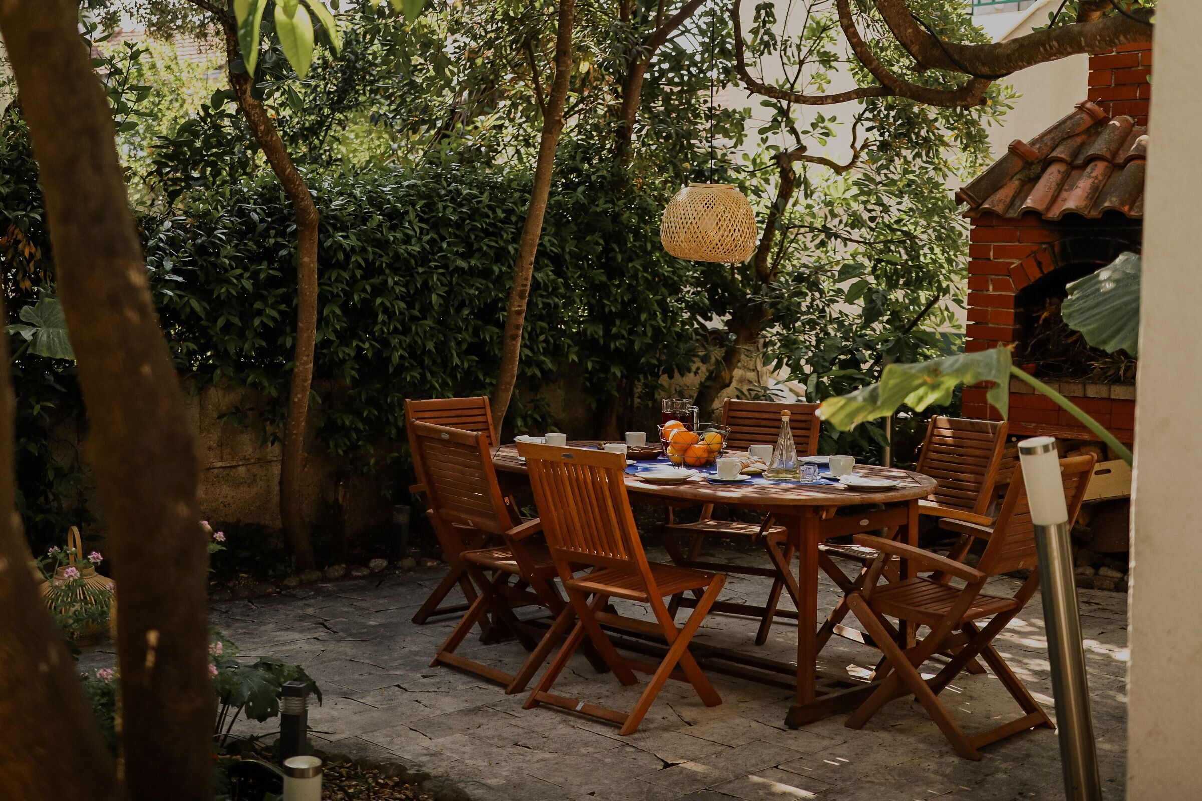 An outdoor dining area with a round table, wooden chairs, and a hanging light fixture.