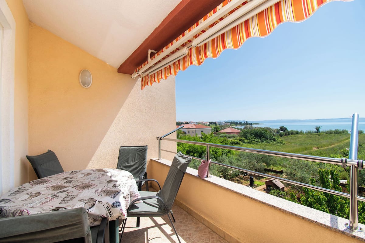 A balcony with a table and chairs, a view of the sea, and a railing.