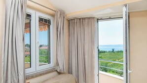 Une chambre à coucher avec un lit, une fenêtre avec des rideaux et une vue sur un paysage verdoyant, visible à travers une porte-fenêtre coulissante.