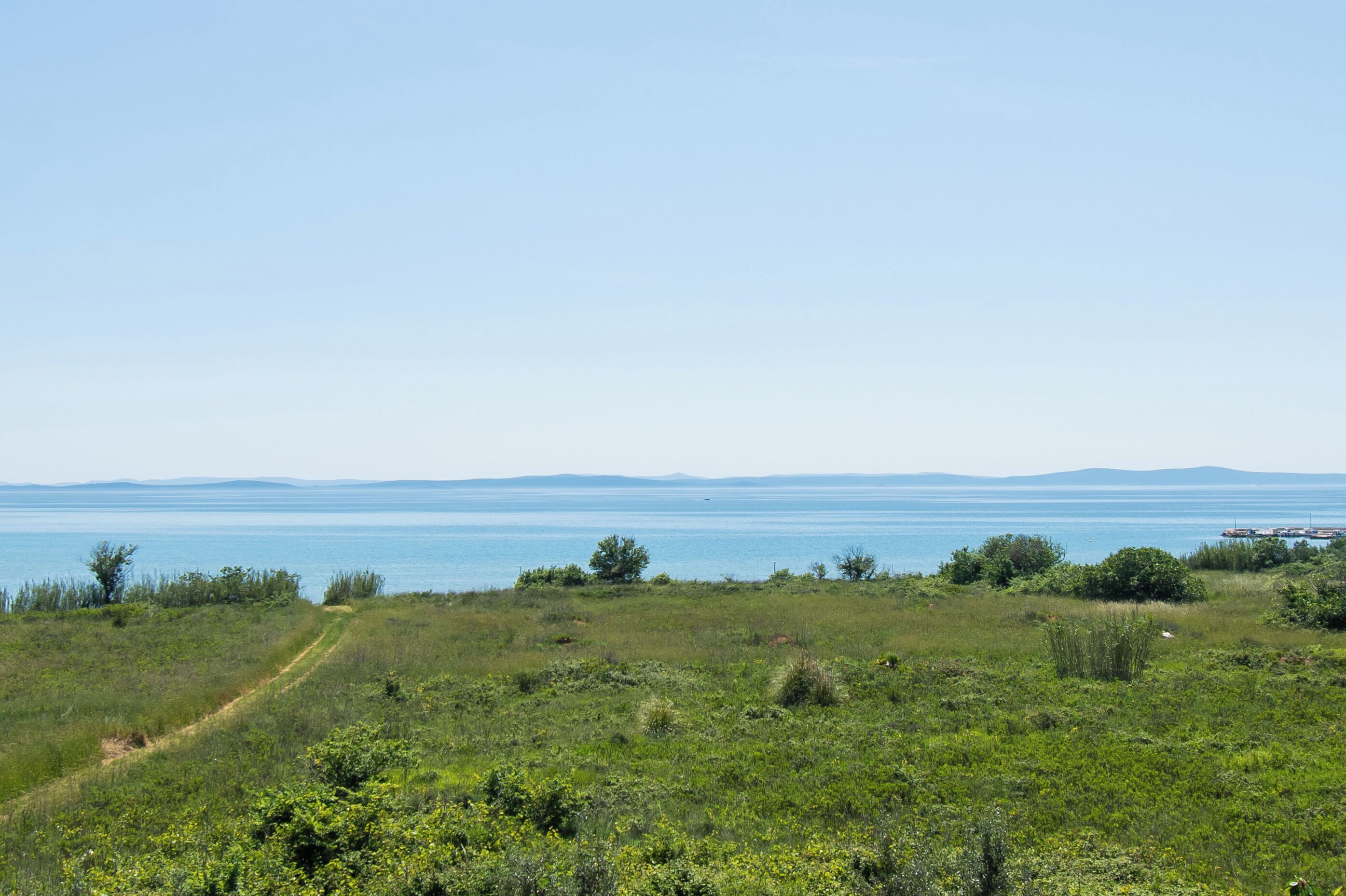 Eine Küstenlandschaft mit blauem Himmel, einer grünen Wiese und einer weiten Aussicht auf Meer und Berge.