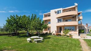 Un immeuble résidentiel à plusieurs étages, doté d’un jardin, d’un espace extérieur aménagé et surplombant un ciel bleu dégagé.