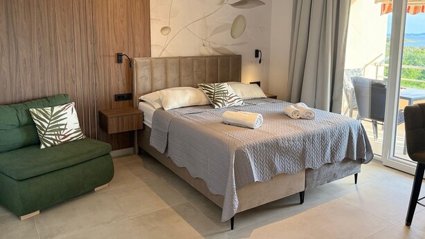 Une chambre d’hôtel moderne avec un lit, un canapé vert, un mur décoratif en bois et une vue sur l’extérieur.