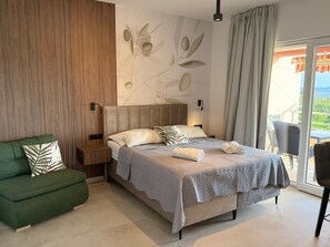 A modern hotel room with a bed, a green sofa, a wooden accent wall, and a view of the outdoors. - Apartments Stefa (Privlaka)