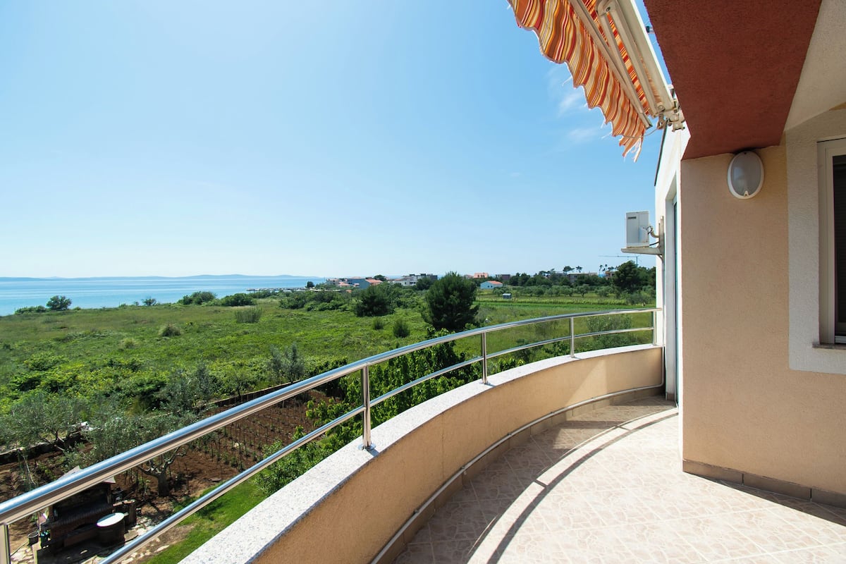A balcony with a metal railing overlooking a green landscape and a body of water.
