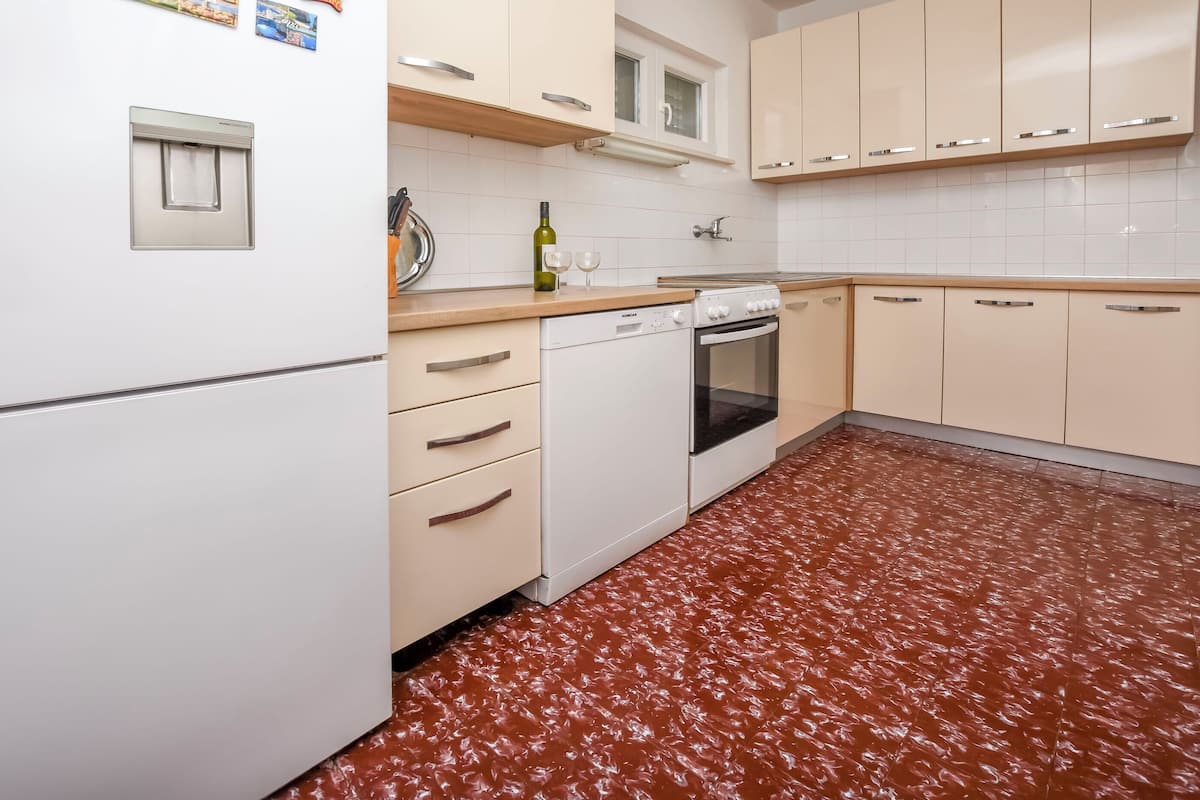 A kitchen with white cabinets, a dishwasher, an oven, and a red patterned floor.