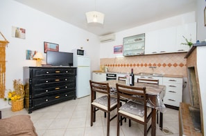A compact kitchen with a dining area, white cabinets, a microwave, a refrigerator, and a tiled backsplash. - Apartment Dijana (Blato)