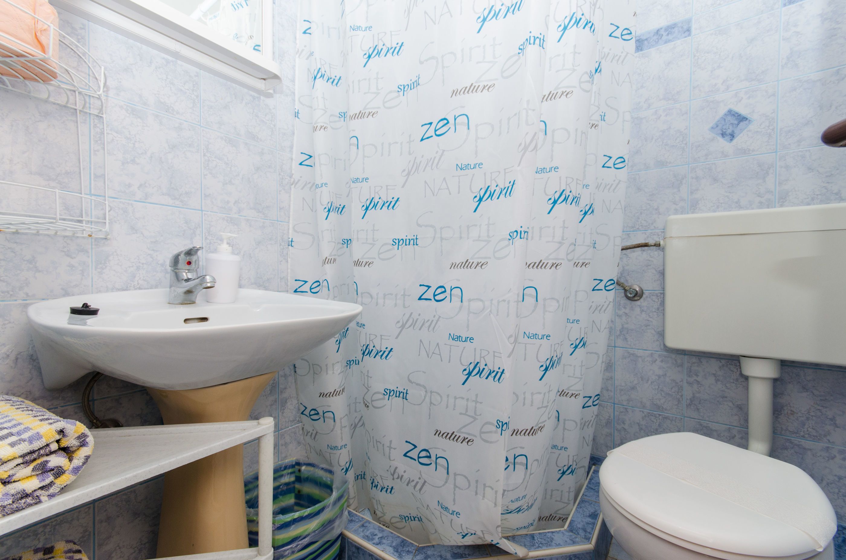 A bathroom with a sink, toilet, and shower curtain with words like 'spirit' and 'nature' printed on it.