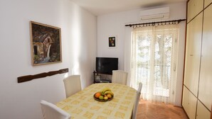 Un coin repas avec une table dressée pour deux personnes, un tableau au mur, un téléviseur et une armoire.