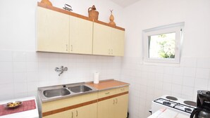 Une cuisine avec des armoires blanches, un évier en acier inoxydable, une cuisinière et une fenêtre.