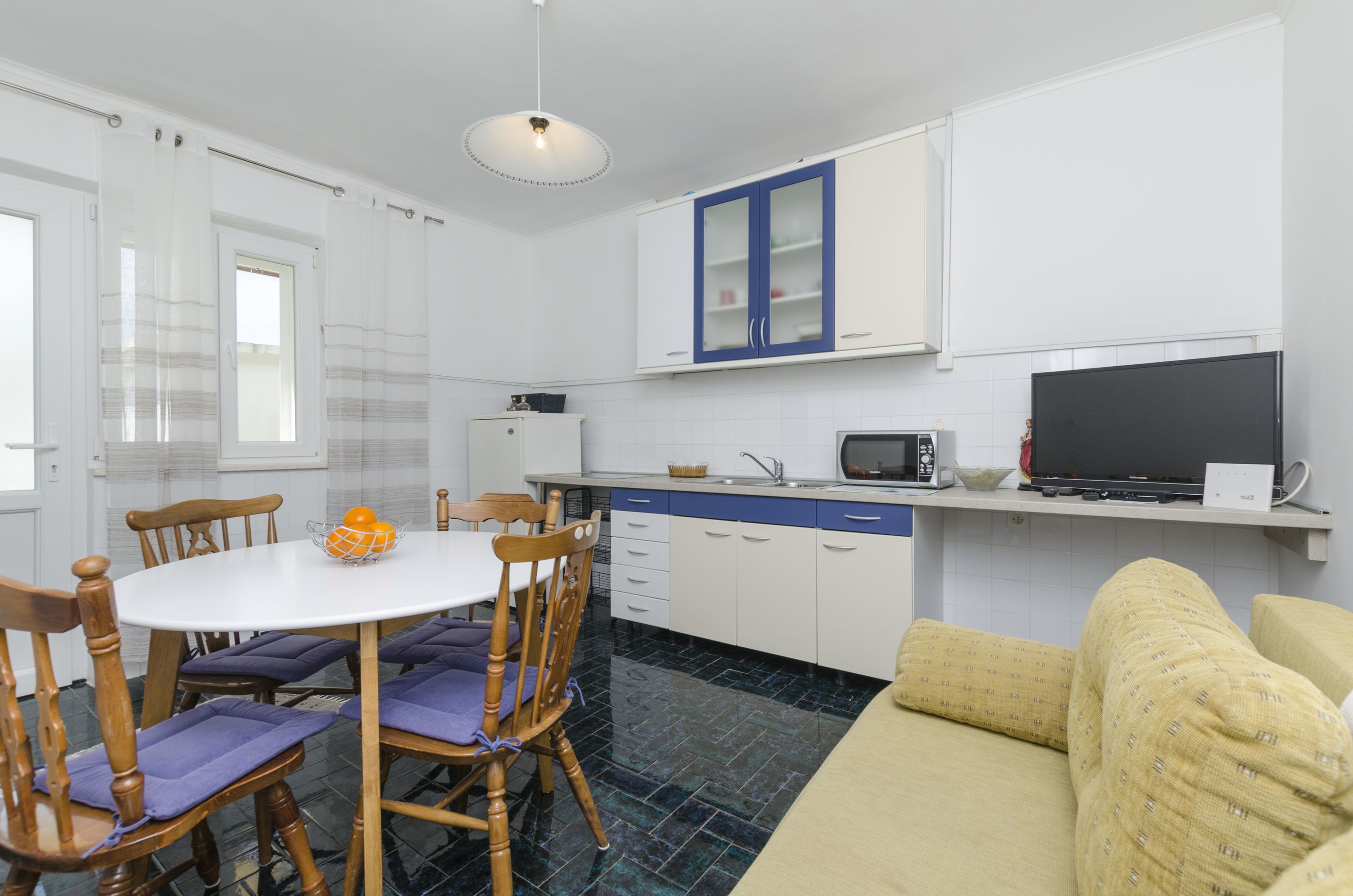 A compact kitchen with white cabinets, a microwave, and a sink. There is a dining table with chairs and a yellow sofa.