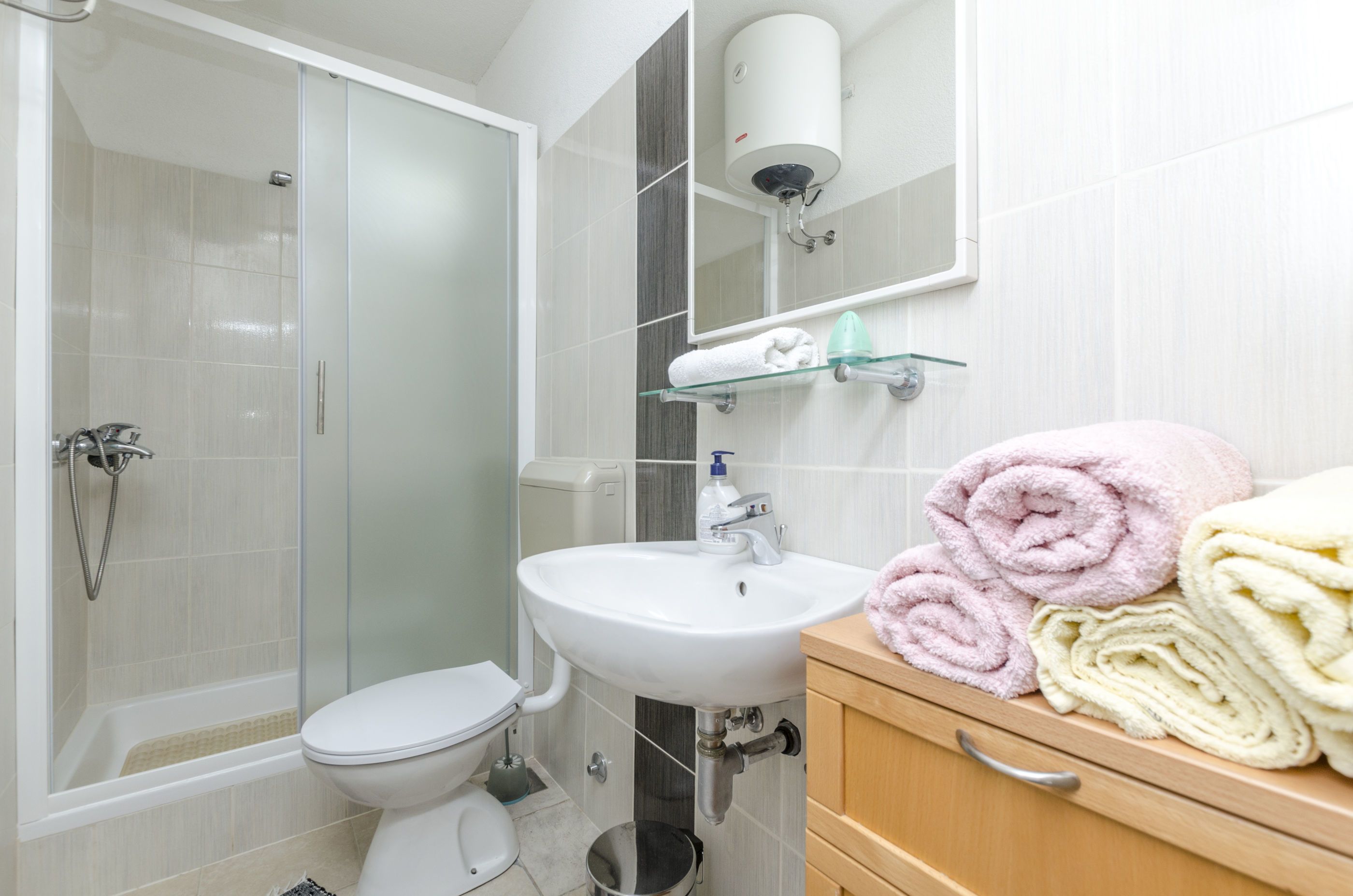 A modern bathroom with a glass shower enclosure, a white sink, and a wooden vanity with towels.