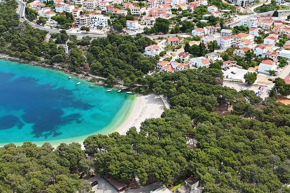 Vista aerea di una località costiera con spiaggia, vegetazione fitta e edifici residenziali.