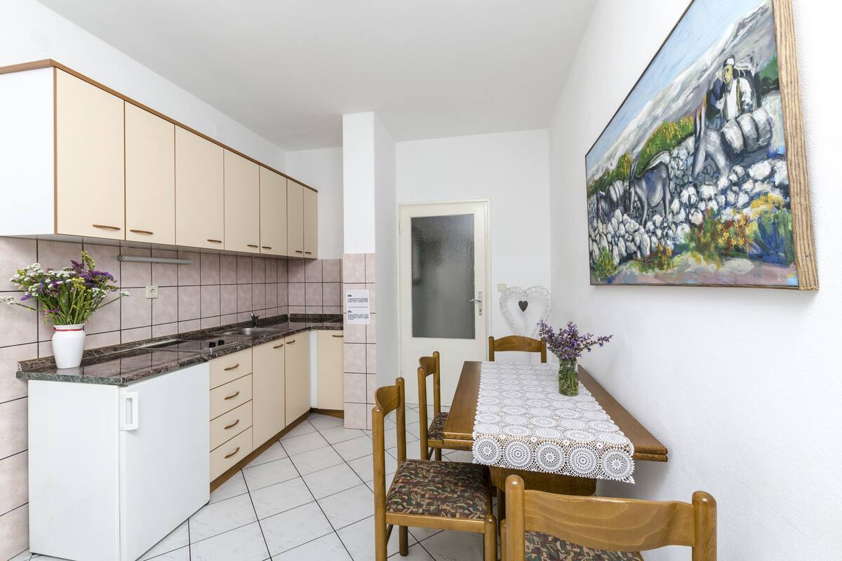 A compact kitchen with beige cabinets, a white refrigerator, and a dining table with a lace tablecloth.