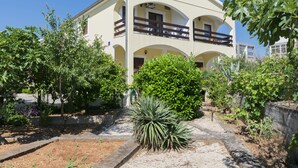 A two-story building with a balcony, surrounded by greenery and a garden area.