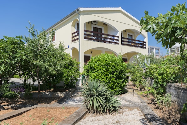 A two-story building with a balcony, surrounded by greenery and a small garden area. - Apartments Grozdana (Primosten)