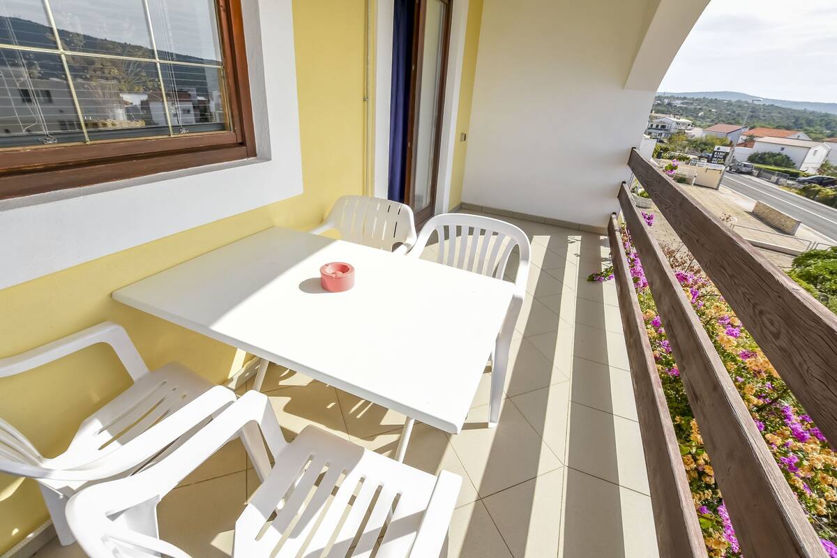 A balcony with a white table and chairs, a wooden railing with flowers, and a view of the city.