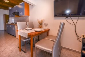 A modern kitchen with grey cabinets, a wooden table, and a TV mounted on the wall. - Apartments Grozdana (Primosten)