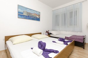 Camera d'albergo con due letti, un quadro raffigurante una veduta costiera, una finestra con tende leggere e un comodino con una lampada.