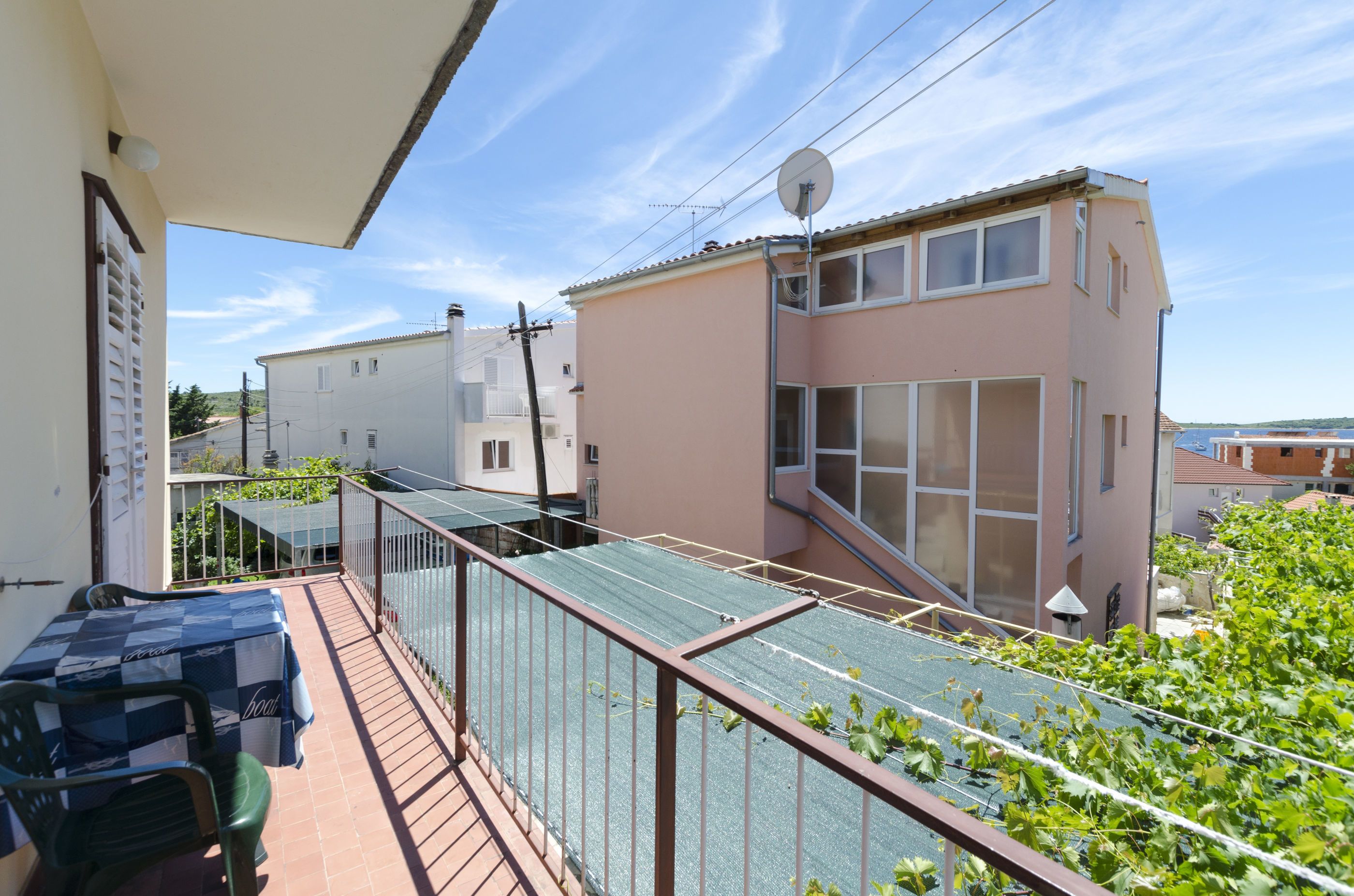 A balcony with a table and chairs, a glass railing, and a view of neighboring buildings.