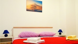 A neatly made bed with red bedding, two purple pillows, and a mountain landscape painting above it. - Apartments Graciela (Zaklopatica)