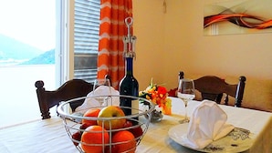 A dining table with a fruit bowl, wine bottle, and glasses, set against a window with curtains. - Apartments Graciela (Zaklopatica)