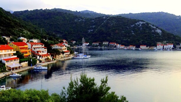 A coastal town with buildings along the waterfront, a marina with boats, and hills in the background. - Apartments Graciela (Zaklopatica)