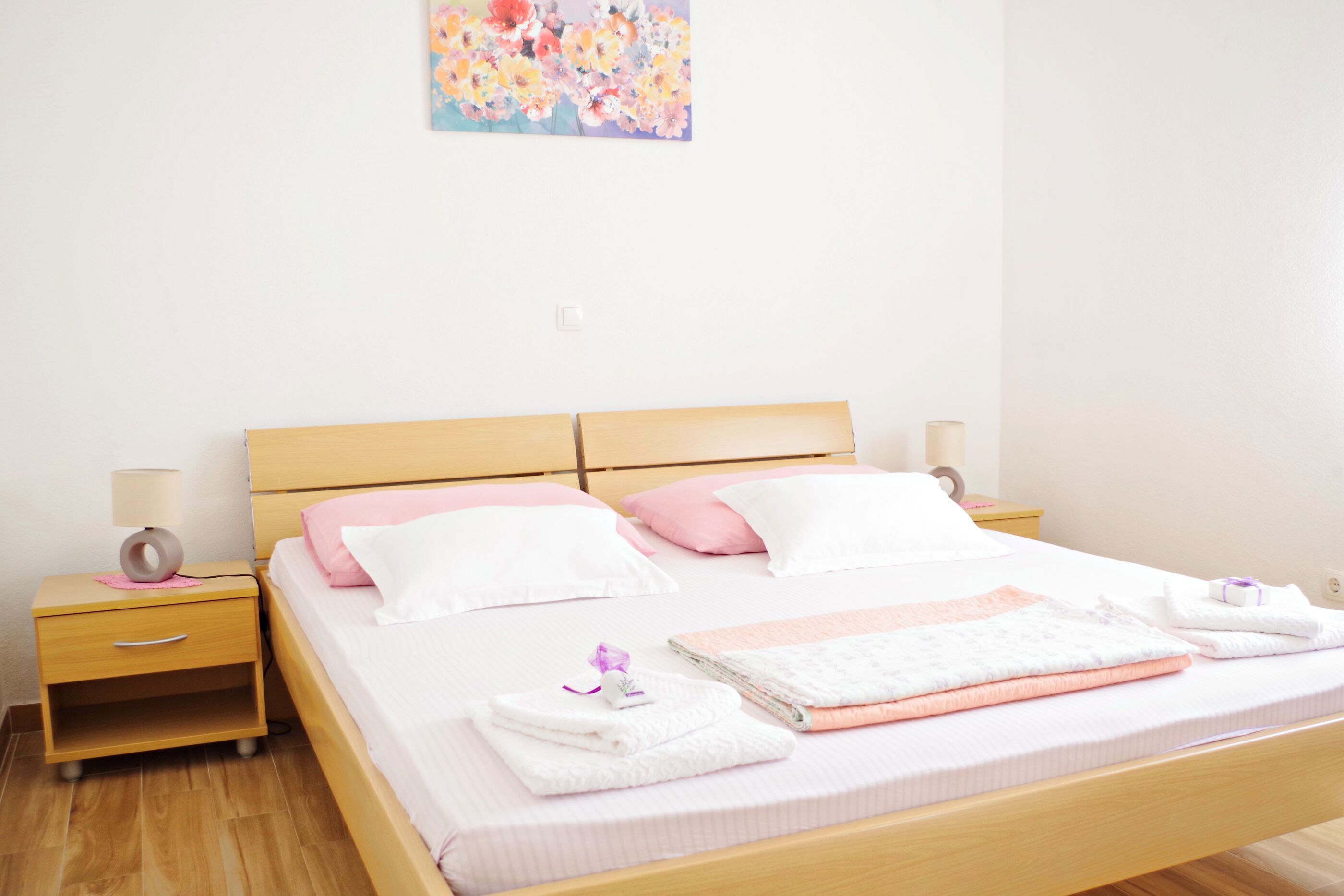 A neatly made bed with pillows, a bedside table with a lamp, and a wall-mounted painting.