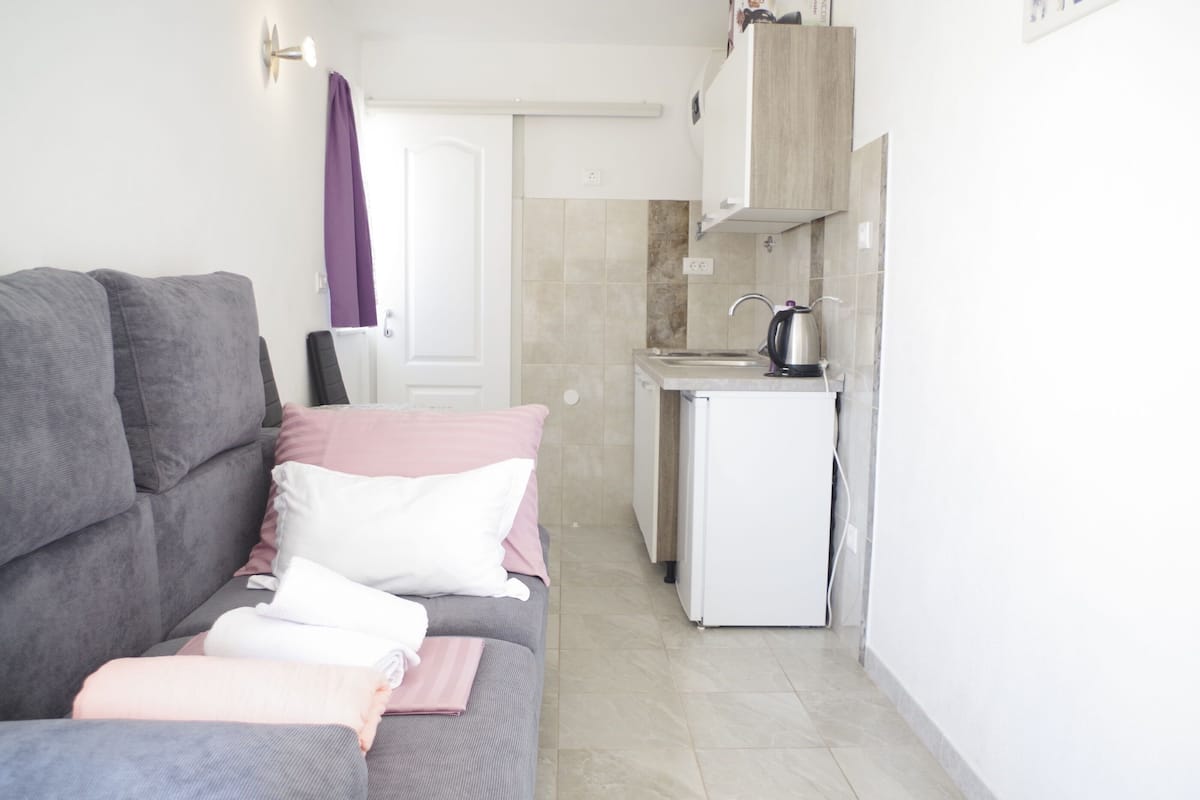 A compact living space with a sofa, a small kitchenette, and a door leading to another room.