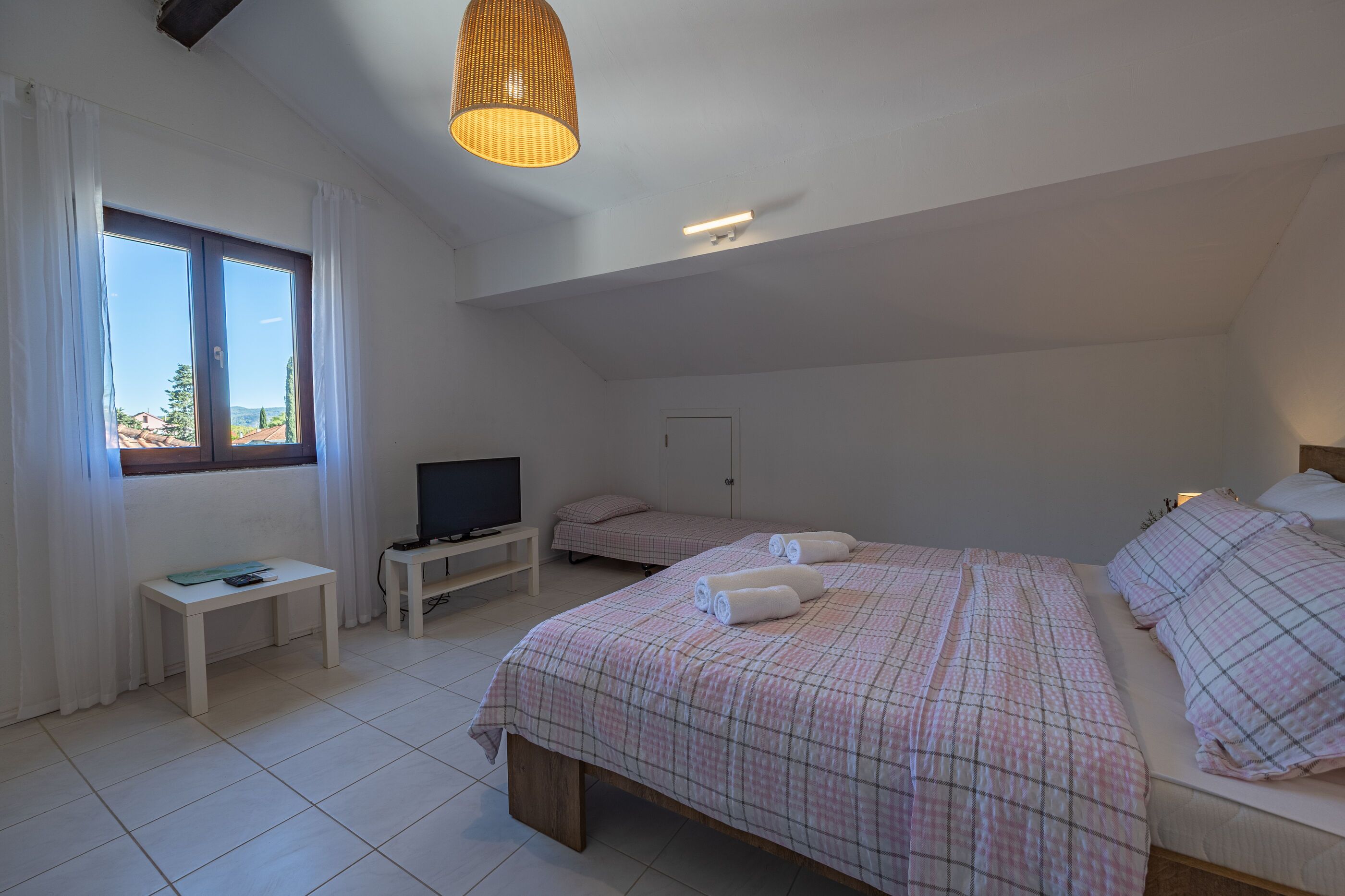 A bedroom with two beds, a TV, a small table, and a window with curtains.