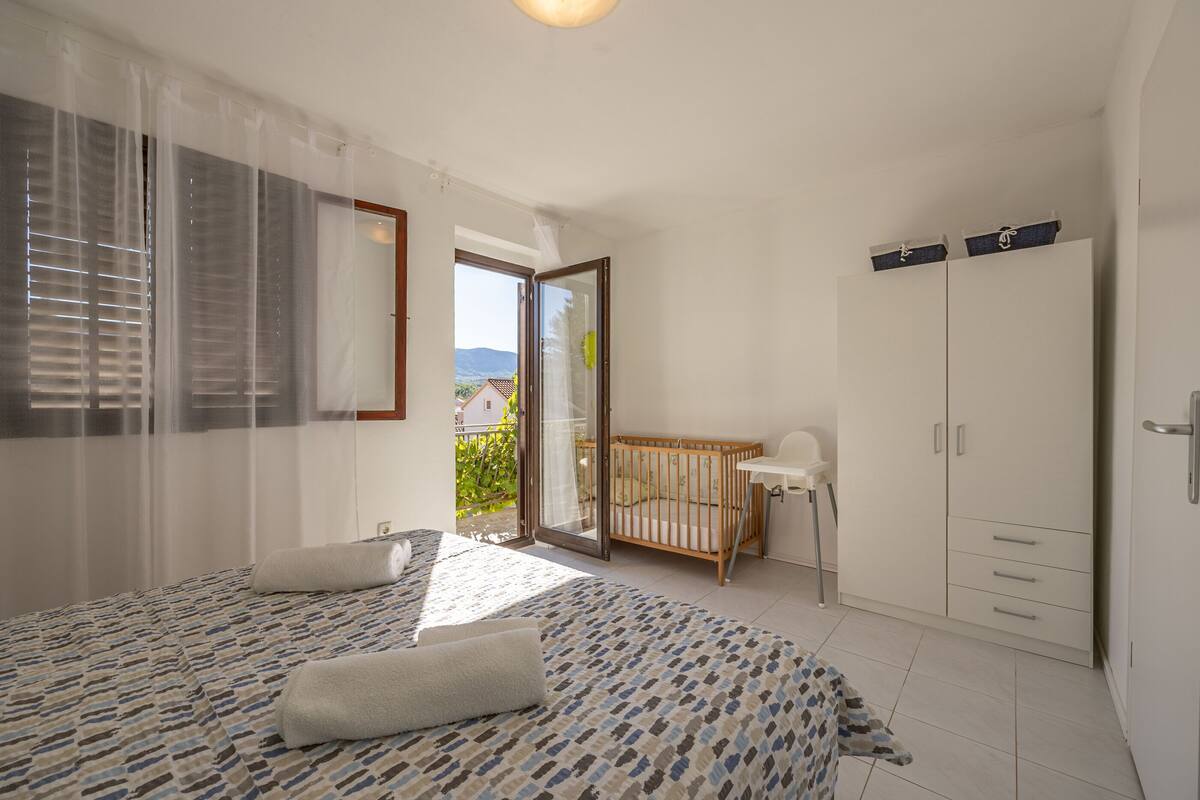 A bedroom with a bed, a crib, a wardrobe, and a balcony with a view.