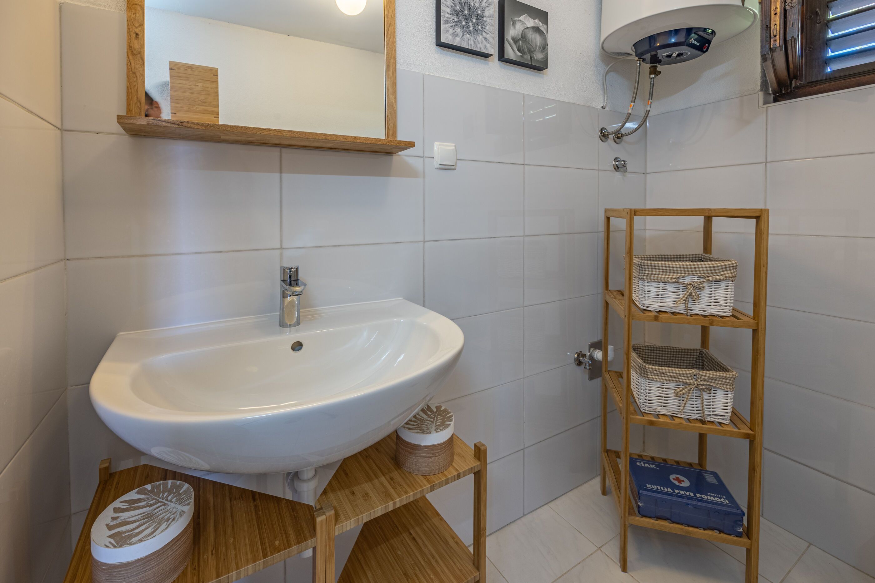 Un baño con un lavamanos blanco, una repisa de madera con cestas, y un espejo sobre el lavamanos.