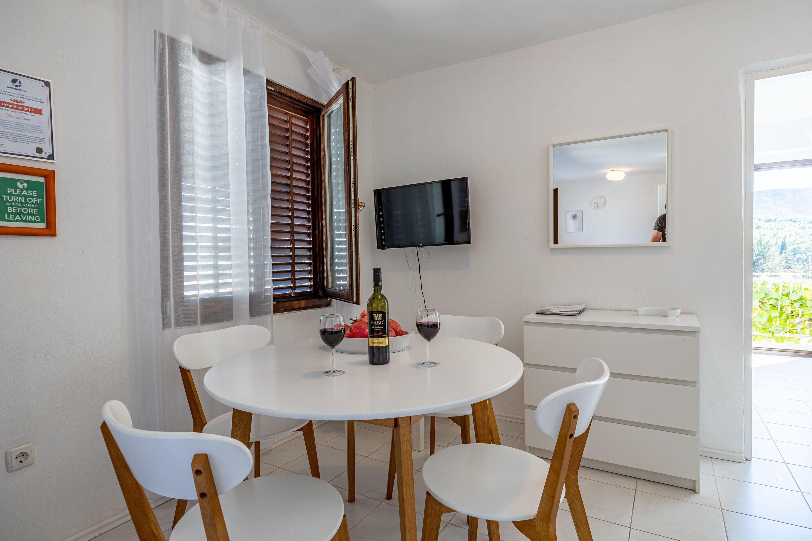 A dining area with a round table, white chairs, a bottle of wine, and a bowl of fruit.