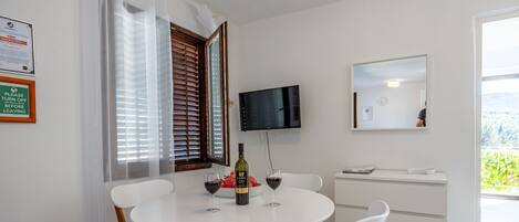 A dining area with a round table, white chairs, a bottle of wine, and a bowl of fruit.