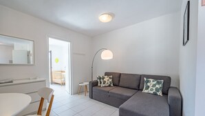 Una sala moderna con un sofá gris, una mesa de comedor blanca y una mesita auxiliar.