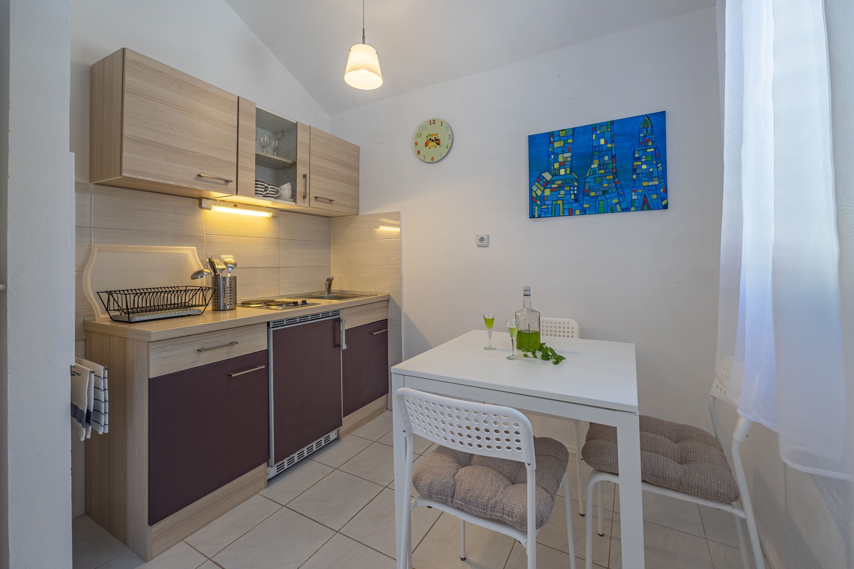 A compact kitchen with wooden cabinets, a white countertop, and a dining area with a white table and chairs.