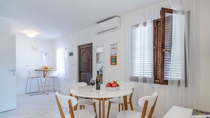 Un comedor con una mesa redonda, sillas blancas y un cuenco de fruta.