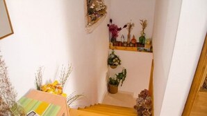 Eine enge Holztreppe führt zu einer Empore. An der Wand befinden sich Regale mit verschiedenen Dekorationen und Pflanzen.