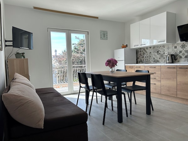 Un salon moderne avec un canapé, une table à manger et des chaises, une cuisine équipée d’armoires et un téléviseur fixé au mur.