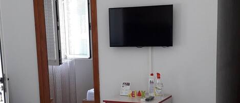 A living room with a sofa, a television mounted on the wall, a small table with items, and a door leading to another room.
