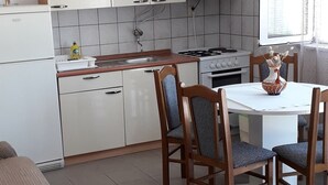 Eine kleine Küche mit weißen Schränken, einem Herd und einem Essbereich mit einem runden Tisch und Holzstühlen.