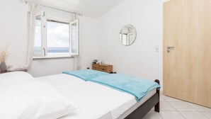 Ein Schlafzimmer mit zwei Betten, einem Holzschrank, einem Nachttisch, einem Spiegel und einem Fenster mit Vorhängen.