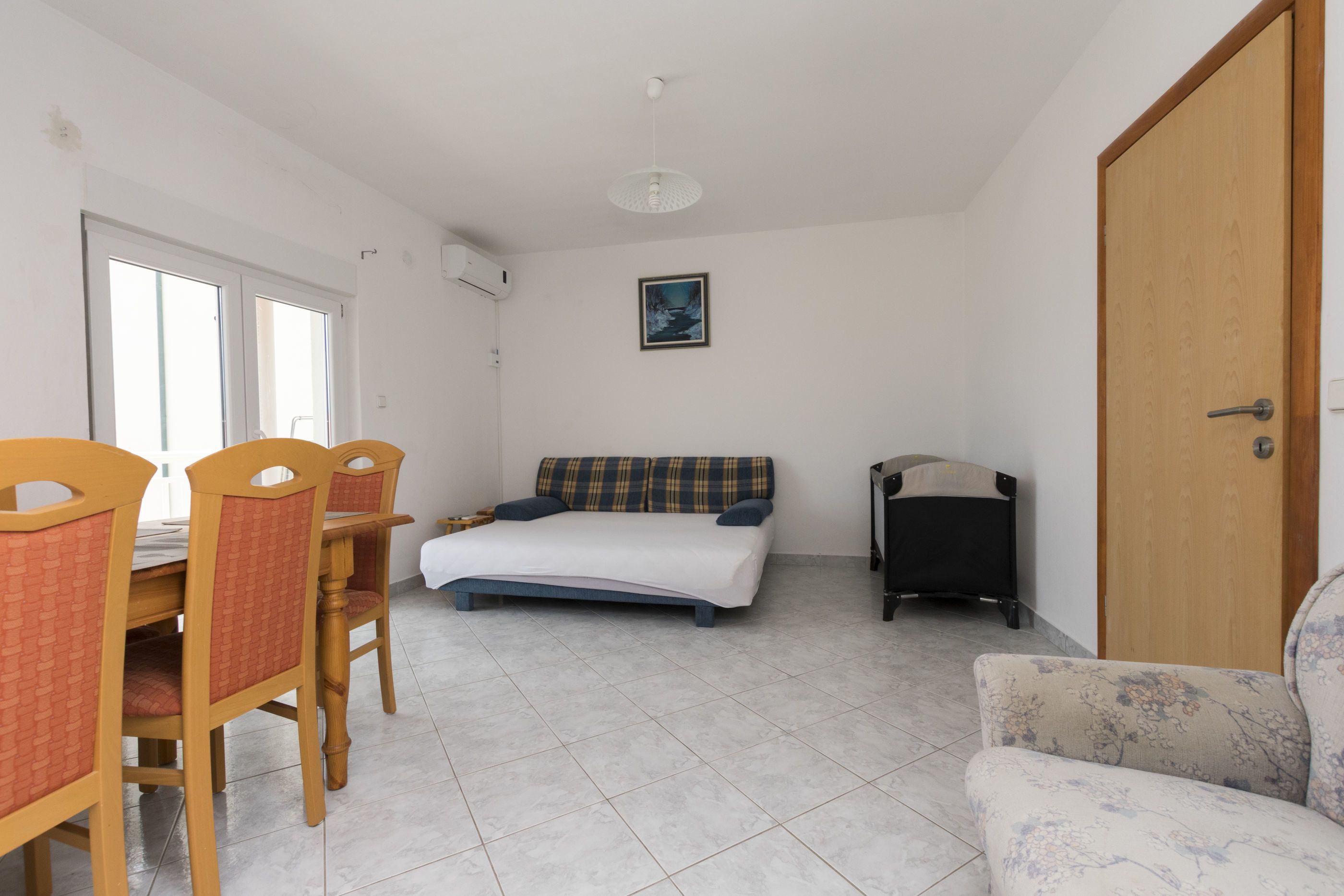 A room with a bed, a sofa, a dining table with chairs, and a door.
